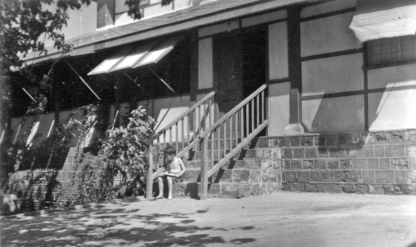 Author as child sitting on steps outside maried quarters building